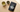 Top-down view of an elegant Japanese-style teacup with green tea, a bowl of loose green tea leaves and cardamom pods, and a bag of Combray tea on a wooden surface