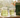 A glass teapot of green tea, a tasting glass of green tea, and a bag of Essentials Bright Green tea on a light wooden countertop in early morning backlit sunlight